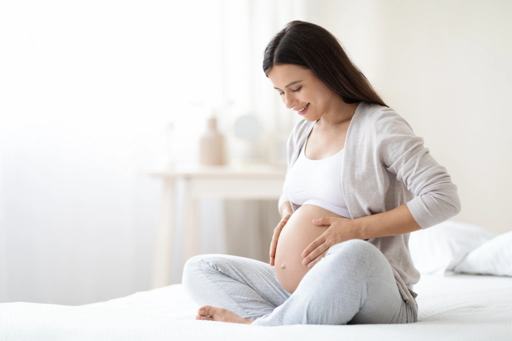 smiling-pregnant-woman-sitting-on-bed-in-her-bedro-2025-03-18-18-11-50-utc.webp